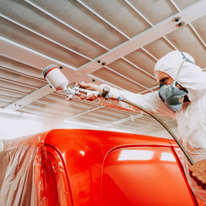 Automotive mechanical engineer painting the body of a red car wi Automotive mechanical engineer painting the body of a red car with special suit