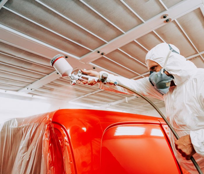 Automotive mechanical engineer painting the body of a red car with special suit